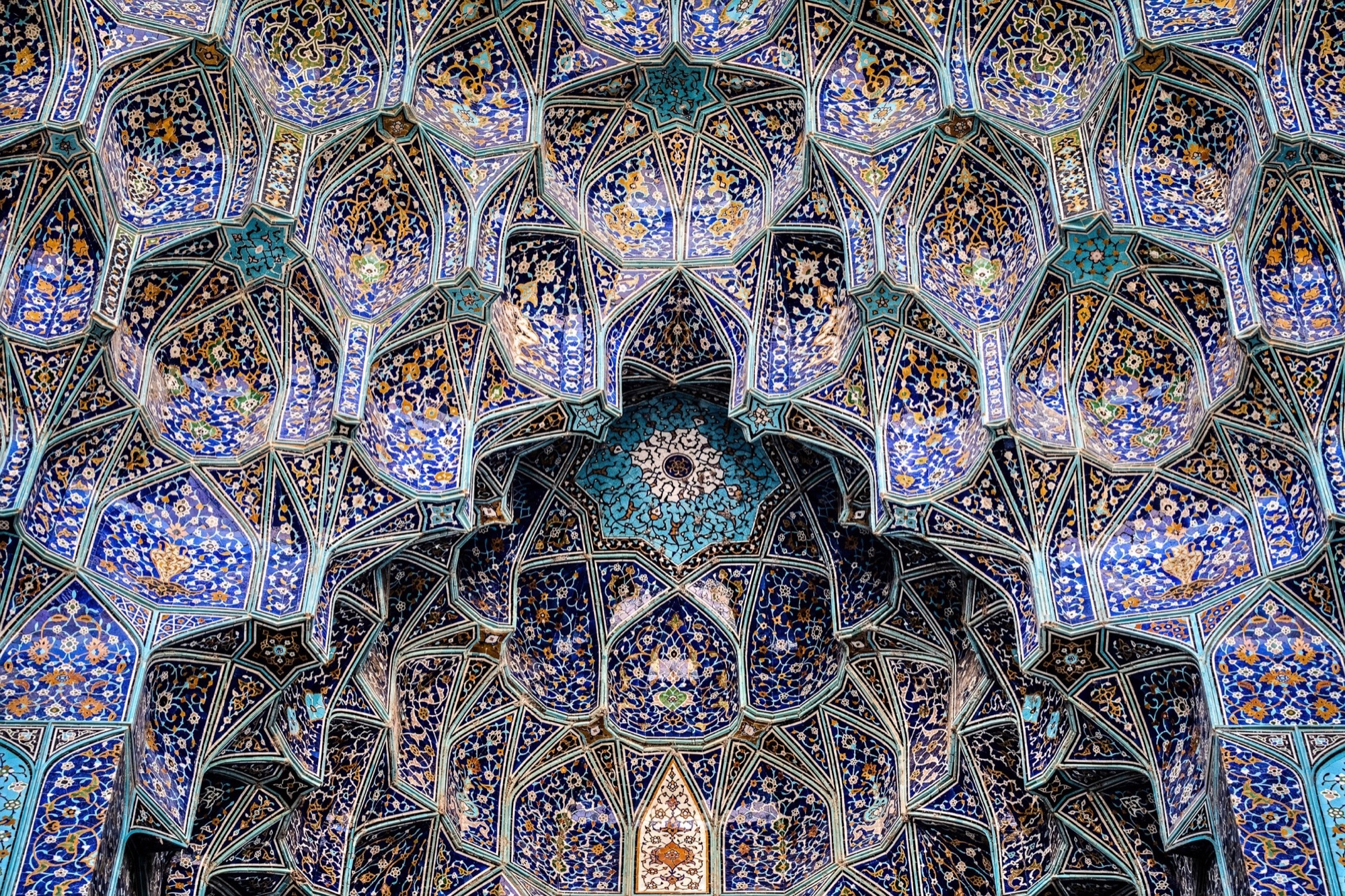 Tiled muqarnas of a Safavid mosque portal in Isfahan, blue and yellow cells converging on turquoise stars.