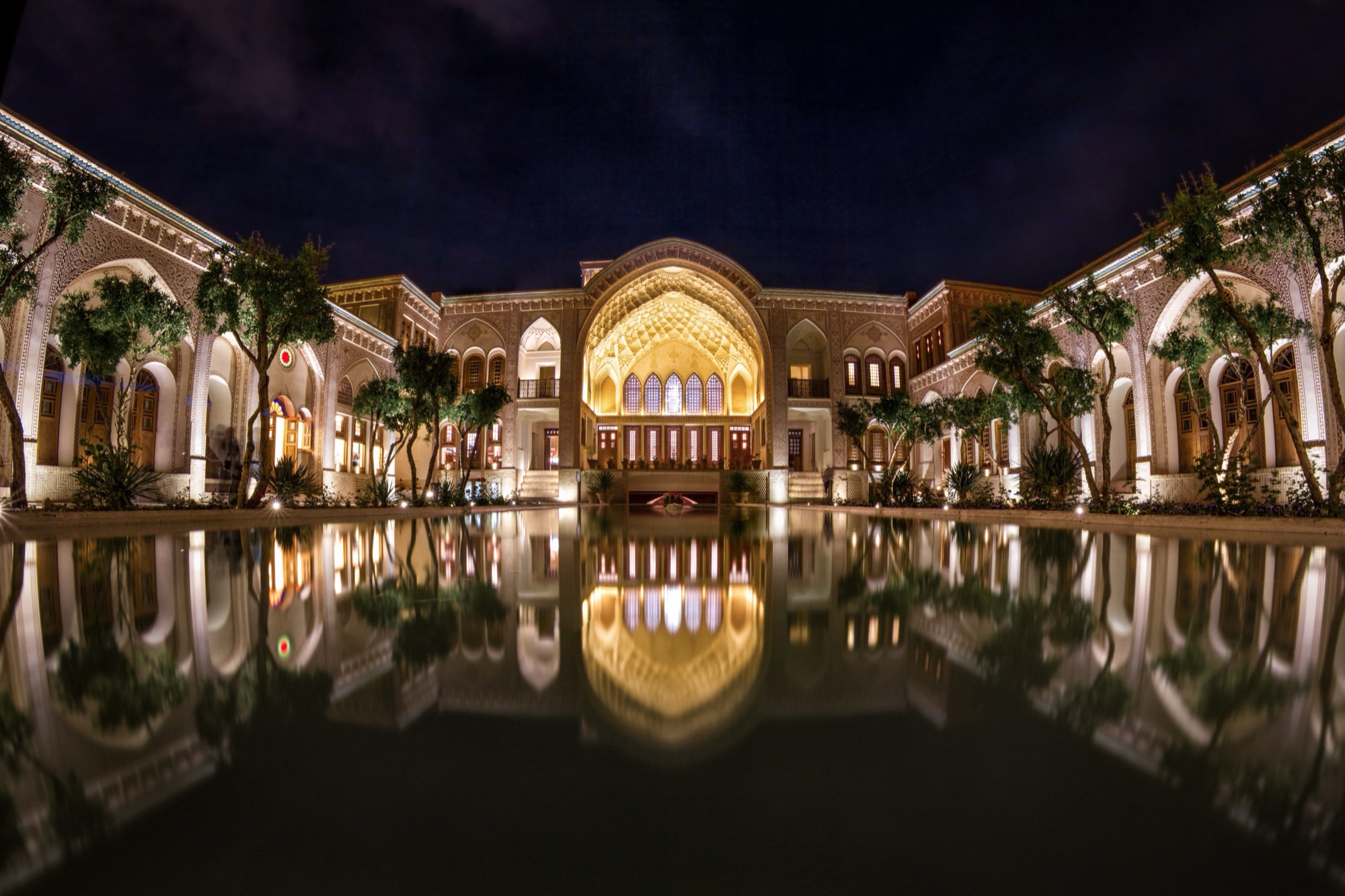 Courtyard house at night, lit iwan reflected in the pool — probably Ameri House