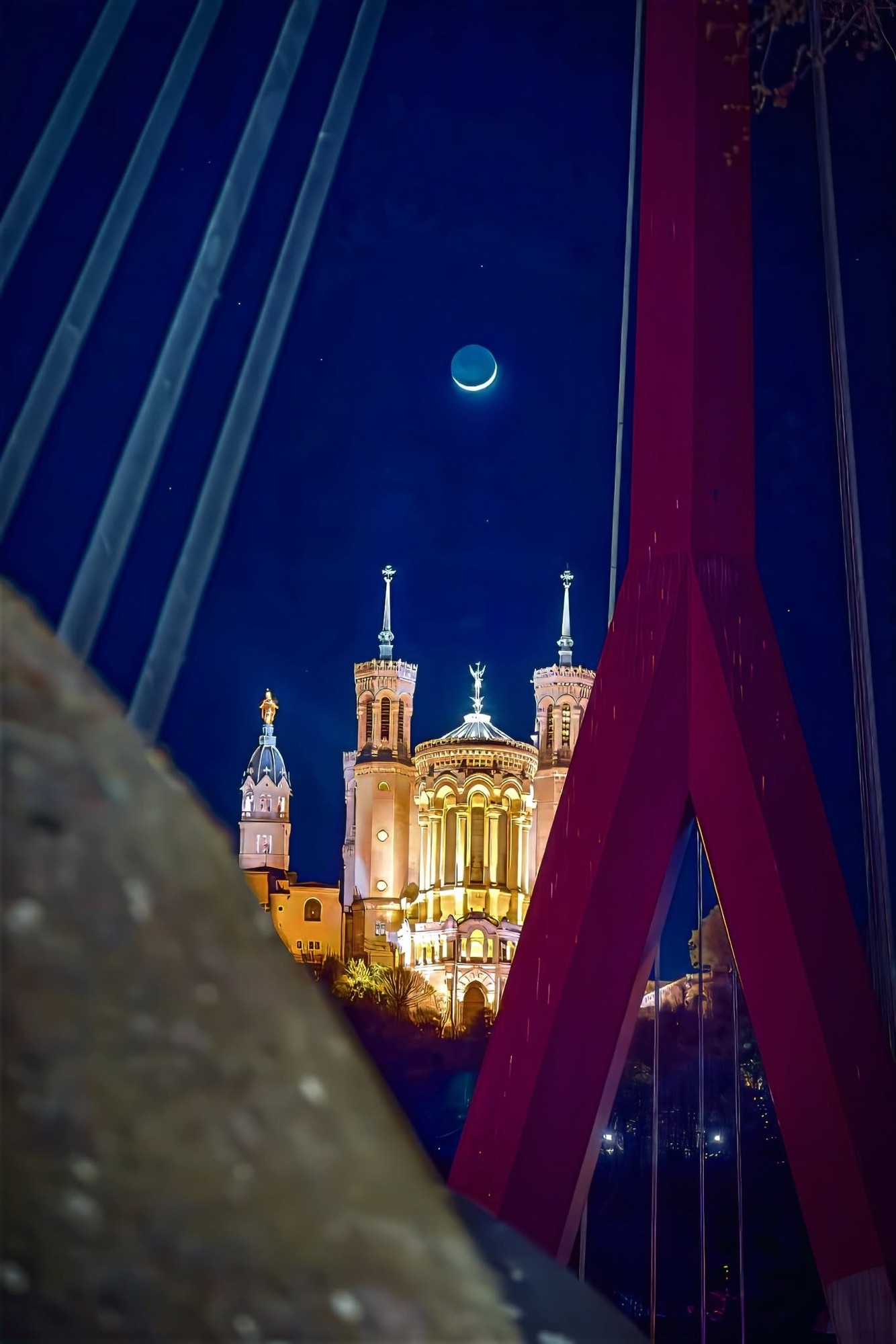Fourvière by moonlight framed by a red footbridge pylon and cables