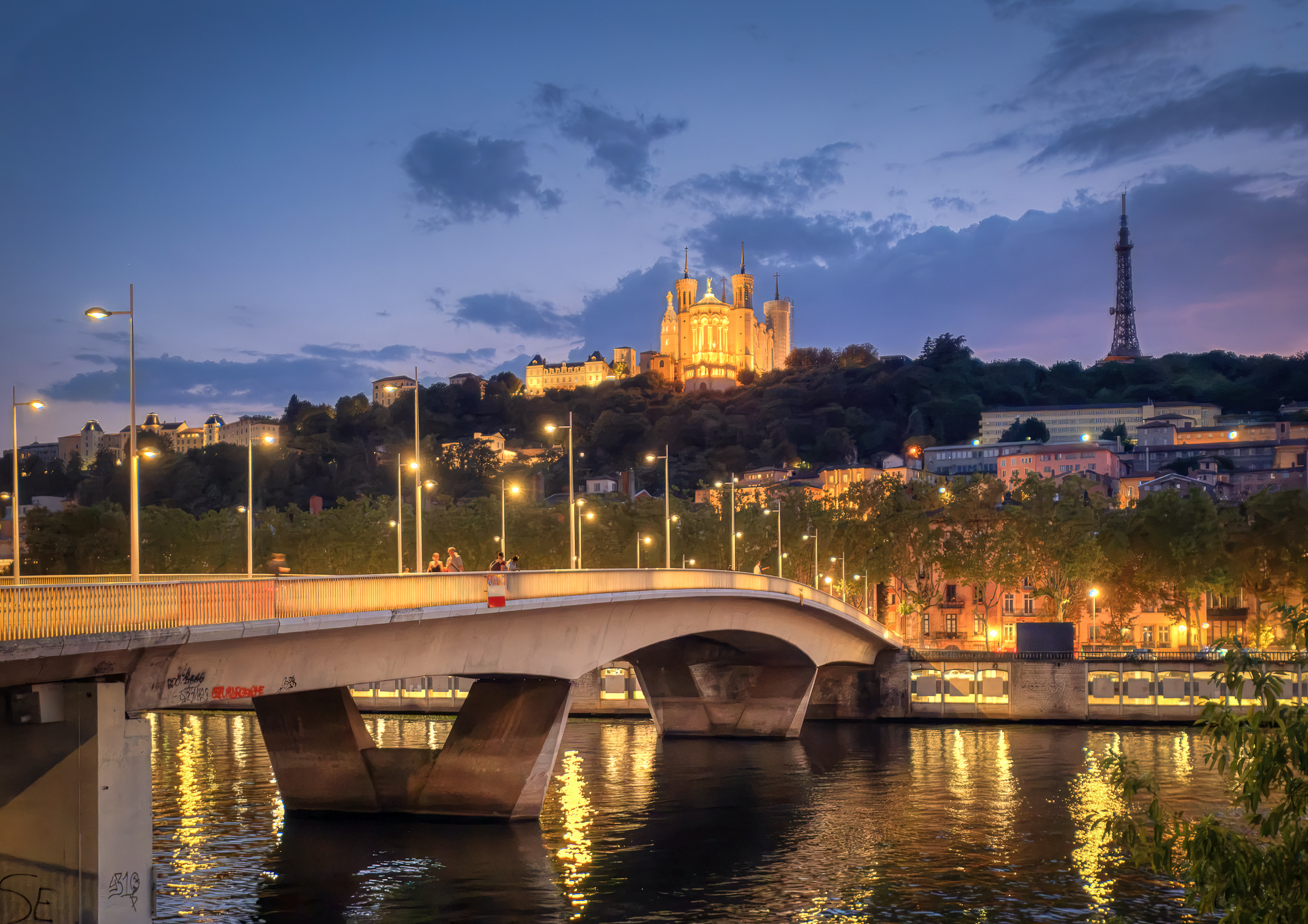 Crépuscule sur la Saône : la courbe du pont Maréchal-Juin sur ses piles en V, les quais illuminés du Vieux Lyon et, sur la colline, la basilique Notre-Dame de Fourvière et la tour métallique éclairées