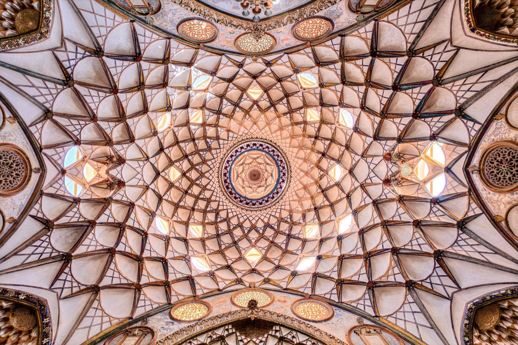A muqarnas vault seen from its centre, its star pattern converging on a central rosette.