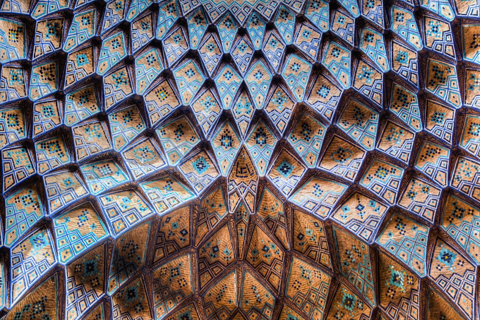 Des alvéoles de muqarnas en céramique turquoise qui ruissellent le long de la voûte d’un portail.