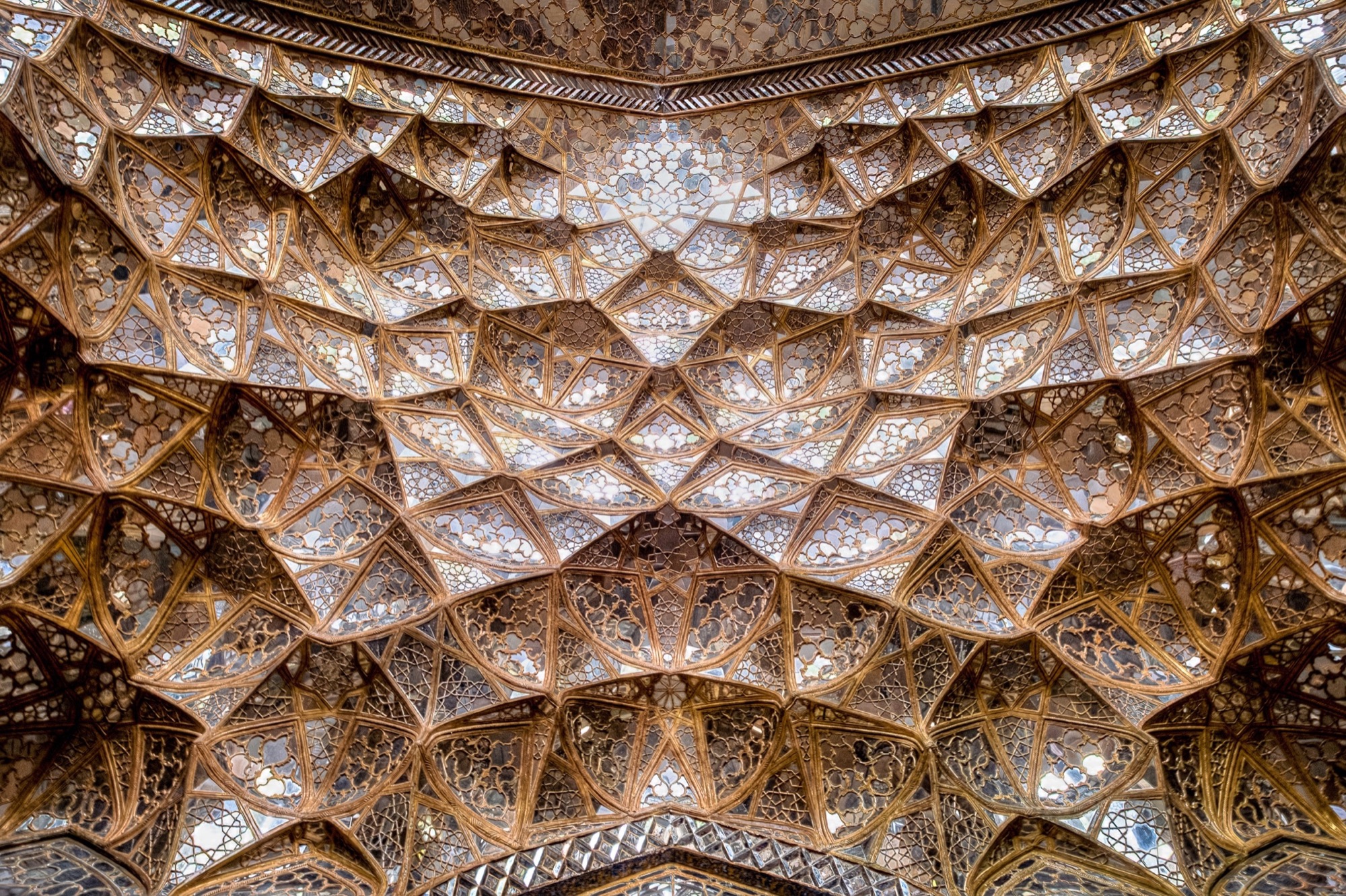 Alvéoles de muqarnas à facettes, scintillant dans une lumière chaude sous un plafond.