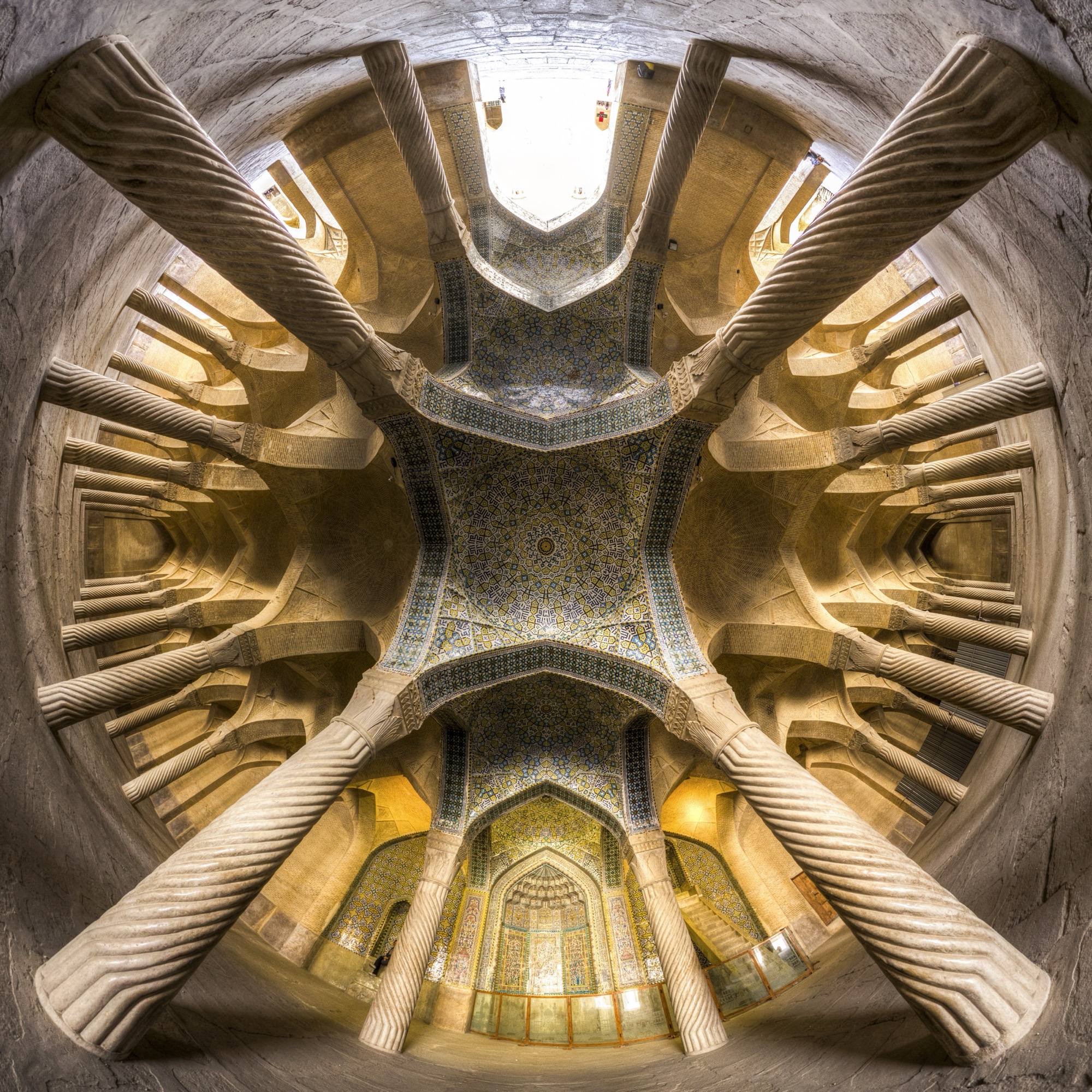 La mosquée Vakil, à Chiraz, vue depuis le sol comme un mandala quadripartite : des colonnes sculptées en spirale rayonnent vers une voûte de céramique, au centre.
